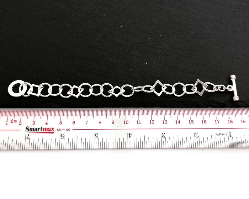 Pu&ograve; includere: Braccialetto d'argento con un design a catena a maglie e maglie di forma quadrata. Il braccialetto misura 17,8 cm di lunghezza.