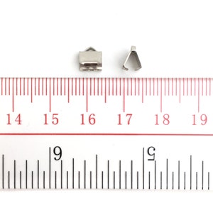 Op de afbeelding: Twee zilveren metalen sluitingen voor het maken van sieraden, gemeten met een liniaal. De sluitingen zijn ongeveer 1,2 cm lang.