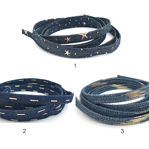 May include: Three rolls of blue denim ribbon with gold accents. The first roll has gold stars, the second has gold lines, and the third has a gold stripe pattern.