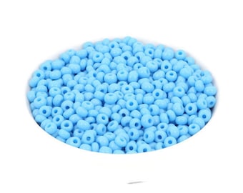 Può includere: Una ciotola piena di perline di semi di colore azzurro chiaro. Le perline sono piccole e rotonde, e sono perfette per l'artigianato.