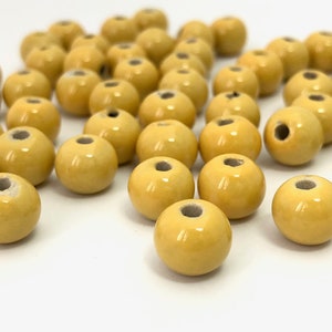 May include: A collection of round, yellow beads with a glossy finish and a hole through the center. The beads are scattered on a white surface, ideal for jewelry making or crafting projects.