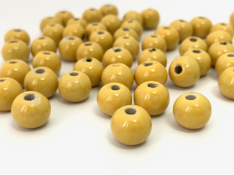 May include: A collection of round, yellow beads with a glossy finish and a hole through the center. The beads are scattered on a white surface, ideal for jewelry making or crafting projects.