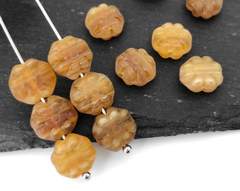 May include: Close-up of several amber-colored flower-shaped beads. The beads are strung on thin silver wires and have a detailed floral design. The beads are made of a translucent material.