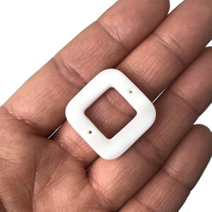 Peut inclure: Pendentif carr&eacute; en c&eacute;ramique blanche avec deux trous. Le pendentif a une ouverture carr&eacute;e au centre.