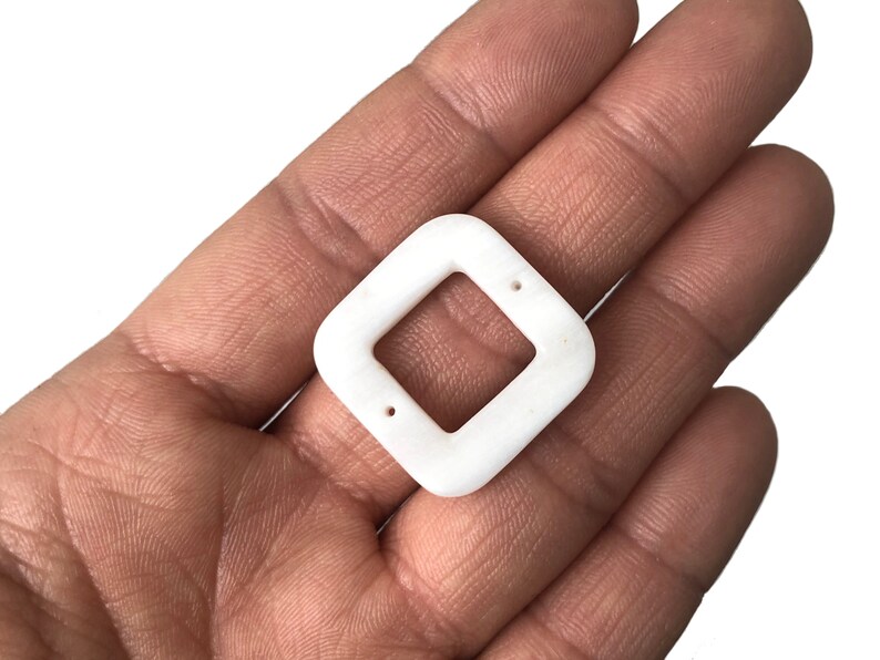 Peut inclure: Pendentif carr&eacute; en c&eacute;ramique blanche avec deux trous. Le pendentif a une ouverture carr&eacute;e au centre.