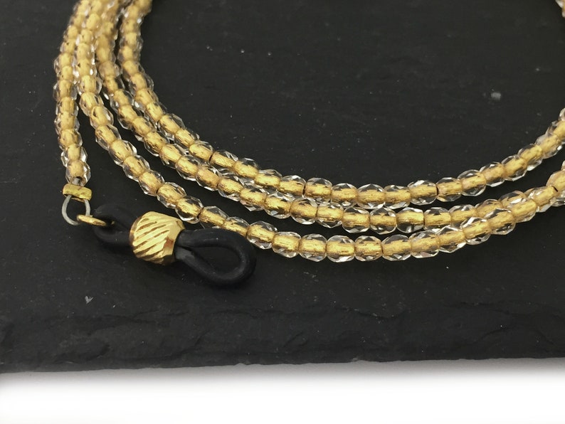 May include: A gold and clear glass beaded eyeglass chain with black rubber ends.