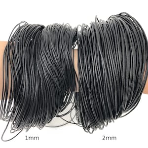Puede incluir: Dos haces de cord&oacute;n negro, uno etiquetado 1 mm y el otro 2 mm. Los cordones est&aacute;n bien enrollados y parecen estar hechos de un material flexible. La imagen est&aacute; sobre un fondo blanco.