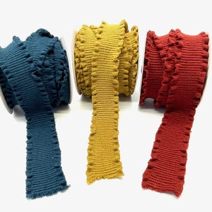 May include: Three spools of ruffled trim in teal, mustard yellow, and burgundy.
