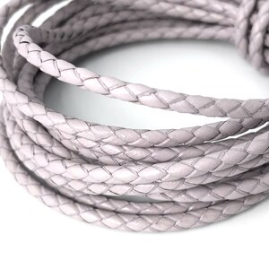 Puede incluir: Primer plano de un rollo de cord&oacute;n de cuero trenzado de color gris claro. El cord&oacute;n es suave y flexible, y tiene un brillo sutil.