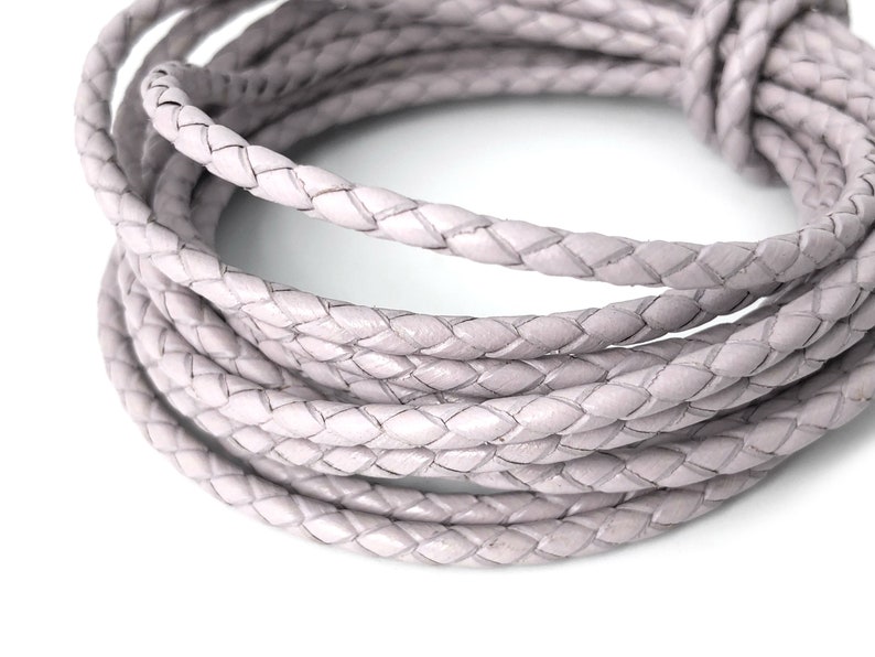 Puede incluir: Primer plano de un rollo de cord&oacute;n de cuero trenzado de color gris claro. El cord&oacute;n es suave y flexible, y tiene un brillo sutil.