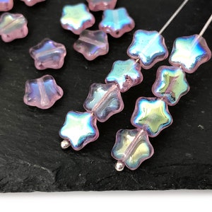 May include: Pink iridescent star-shaped glass beads strung on silver wire. The beads have a light pink color with a rainbow iridescent sheen.