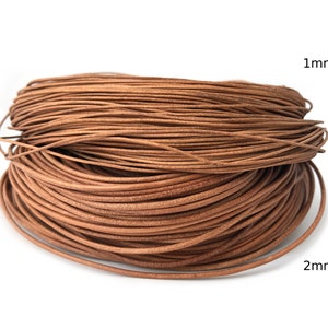Puede incluir: Una bobina de cord&oacute;n de cuero marr&oacute;n, probablemente para manualidades o joyer&iacute;a. El cord&oacute;n parece tener aproximadamente 1 mm y 2 mm de di&aacute;metro. La imagen est&aacute; sobre un fondo blanco, resaltando el color y la textura natural del cuero.