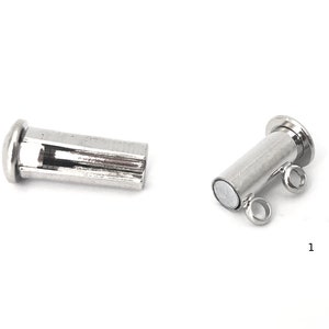 May include: Two silver magnetic clasps for jewelry making. One clasp is a simple cylinder with a flat top. The other clasp has two loops on the side and a flat top.