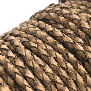 May include: Close-up of a coil of braided leather cord. The cord is a light brown color with a textured surface. The braid is tightly woven, creating a pattern of diagonal lines. This cord is suitable for jewelry making and crafts.