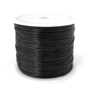 May include: A spool of black thread, tightly wound, sits on a white plastic base. The thread appears to be a matte finish, contrasting with the bright white of the base. The image is a close-up shot against a plain white background.