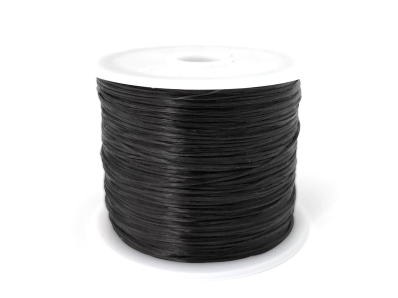 May include: A spool of black thread, tightly wound, sits on a white plastic base. The thread appears to be a matte finish, contrasting with the bright white of the base. The image is a close-up shot against a plain white background.