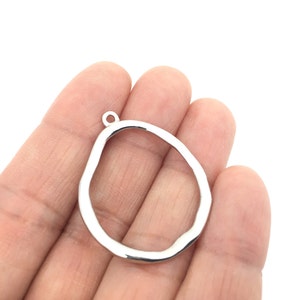 May include: A silver-toned metal pendant charm featuring an irregular, organic, open-frame shape with a smooth, reflective surface. The charm includes a small, circular jump ring at the top for attachment, showcasing a simple, hollow design.