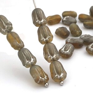 Può includere: Una collana di perline di vetro grigie con un motivo floreale. Le perline sono infilate su un filo d'argento e sono disposte in fila. Nell'immagine ci sono anche diverse perline sciolte.
