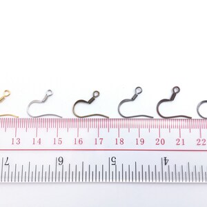 May include: Five earring hooks in different finishes: gold, silver, bronze, black, and gunmetal. The hooks are lined up on a ruler, with the gold hook at the 12-inch mark, the silver hook at the 14-inch mark, the bronze hook at the 16-inch mark, the black hook at the 18-inch mark, and the gunmetal hook at the 20-inch mark.