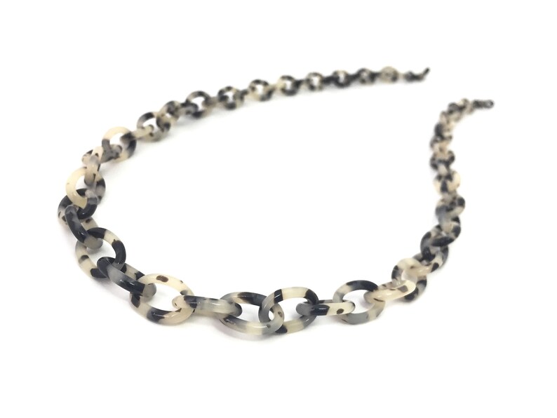May include: A black and white patterned chain necklace made of plastic.