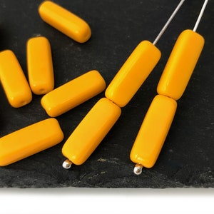 Könnte beinhalten: Eine Gruppe gelber, rechteckiger Glasperlen mit abgerundeten Kanten. Die Perlen sind auf silbernem Draht aufgefädelt.