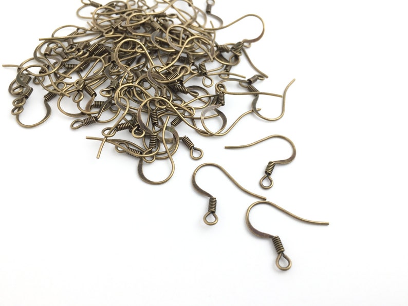 May include: A pile of gold-toned earring hooks, a type of jewelry finding, on a white background.