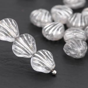 May include: Clear, teardrop-shaped glass beads with a ridged, shell-like design. The beads are strung on a silver wire, with a small silver bead at the end. The beads are translucent, allowing light to pass through.