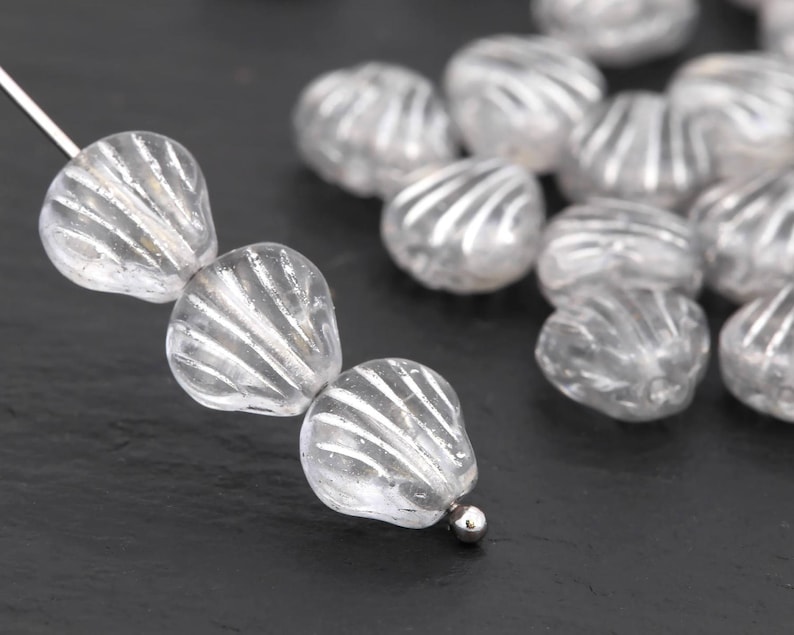 May include: Clear, teardrop-shaped glass beads with a ridged, shell-like design. The beads are strung on a silver wire, with a small silver bead at the end. The beads are translucent, allowing light to pass through.