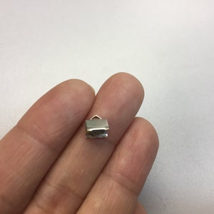Op de afbeelding: Zilverkleurig metalen crimp-eind voor het maken van sieraden. Het crimp-eind is klein en rechthoekig met een afgeronde bovenkant.