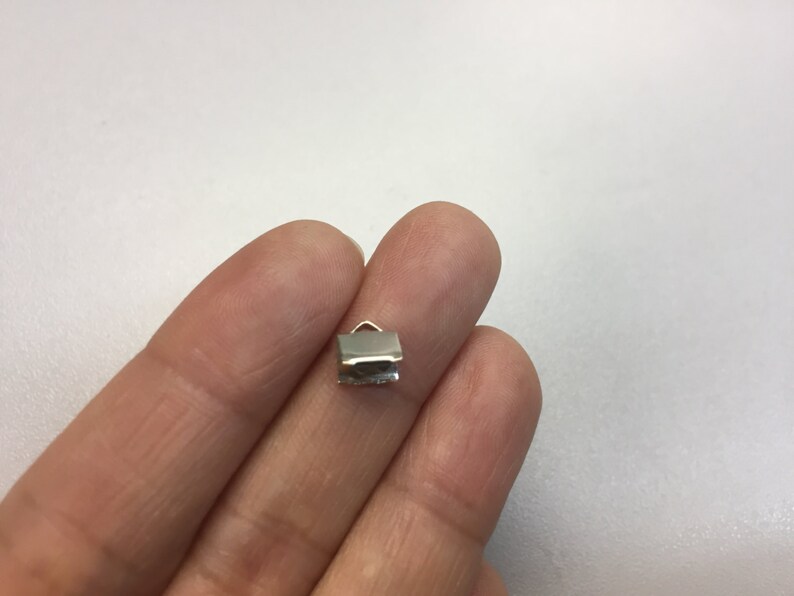 Op de afbeelding: Zilverkleurig metalen crimp-eind voor het maken van sieraden. Het crimp-eind is klein en rechthoekig met een afgeronde bovenkant.