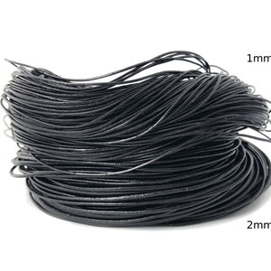 Puede incluir: Una bobina de cord&oacute;n negro, probablemente de cuero o un material similar. La imagen muestra el grosor del cord&oacute;n, con etiquetas que indican di&aacute;metros de 1 mm y 2 mm. El cord&oacute;n est&aacute; sobre un fondo blanco.