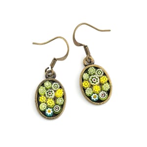 Op de afbeelding: Een paar gouden oorbellen met ovale hangers met een cluster van kleurrijke glazen bloemen. De bloemen zijn geel, groen, wit en blauw.