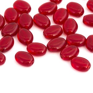May include: A collection of red glass oval beads, scattered on a white surface.