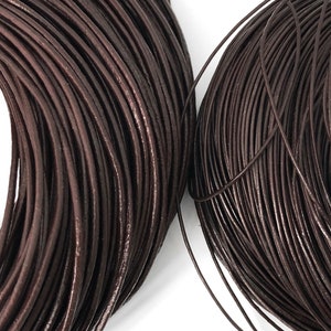 Puede incluir: Primer plano de dos bobinas de cord&oacute;n de cuero marr&oacute;n oscuro. El cord&oacute;n est&aacute; enrollado firmemente, revelando una textura suave y ligeramente brillante. El color es un tono rico y terroso, adecuado para proyectos de joyer&iacute;a o artesan&iacute;a.