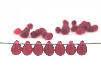 May include: A strand of eight teardrop-shaped glass beads in a deep pink color. The beads are strung on a silver wire.