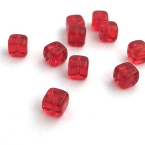 Puede incluir: Un conjunto de cuentas rojas transl&uacute;cidas en forma de cubo con bordes redondeados. Cada cuenta tiene un peque&ntilde;o agujero para ensartar. Las cuentas est&aacute;n dispersas sobre una superficie blanca, mostrando su textura brillante y su color vibrante. Ideal para la creaci&oacute;n de joyas.