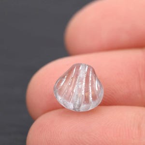 May include: A clear, seashell-shaped bead with vertical ridges. The bead is translucent, allowing light to pass through, and has a rounded, textured surface. This decorative bead is suitable for jewelry making and craft projects.