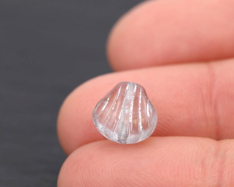 May include: A clear, seashell-shaped bead with vertical ridges. The bead is translucent, allowing light to pass through, and has a rounded, textured surface. This decorative bead is suitable for jewelry making and craft projects.