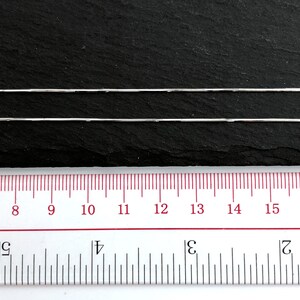 May include: Two silver-colored snake chains are displayed against a dark background. A ruler with inch markings is positioned below the chains, showing measurements from 7 to 16 inches. The chains are thin and reflective.