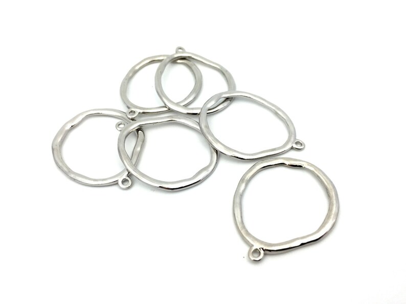 May include: A collection of five silver-toned metal rings with an irregular, organic shape. Each ring features a small, circular loop attached to the outer edge, designed for connecting components. The surface of the metal has a smooth, reflective finish.