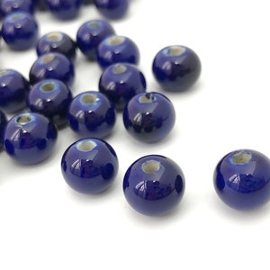 May include: A collection of glossy, dark blue ceramic beads. Each bead is round with a small hole and a lighter blue-grey area around the hole. The beads are scattered on a white surface.