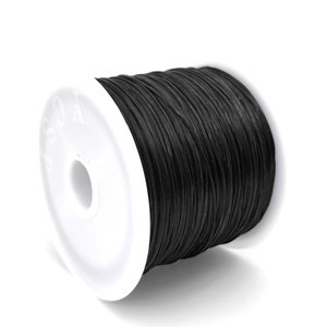 May include: A spool of black cord, tightly wound and ready for use. The cord is a solid black color and appears to be made of a durable material. The spool has a white plastic base with a central hole.