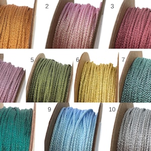 May include: Ten spools of metallic thread, each wound on a cardboard spool. The spools are arranged in three rows of three, with one spool in the bottom row. The thread colours are gold, pink, burgundy, lavender, olive green, gold, teal, light blue, silver, and green.