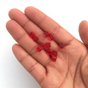 Puede incluir: Una mano que sostiene varias peque&ntilde;as cuentas cuadradas rojas transl&uacute;cidas. Las cuentas son de color uniforme y parecen estar hechas de vidrio o un material similar. Las cuentas est&aacute;n dispersas por la palma.