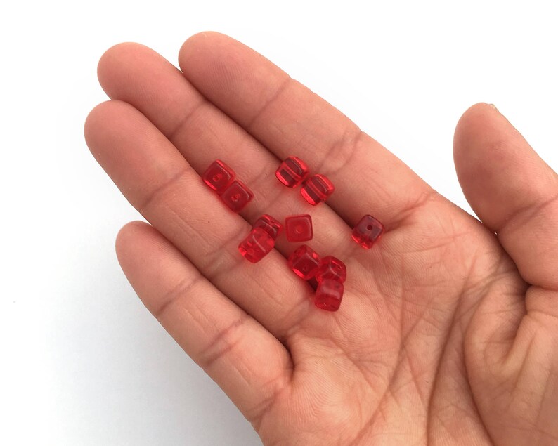 Puede incluir: Una mano que sostiene varias peque&ntilde;as cuentas cuadradas rojas transl&uacute;cidas. Las cuentas son de color uniforme y parecen estar hechas de vidrio o un material similar. Las cuentas est&aacute;n dispersas por la palma.
