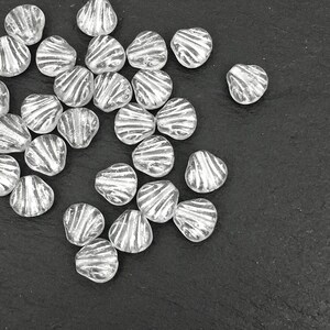 May include: A collection of clear, heart-shaped beads with a silver, striped design. The beads are scattered on a dark surface, showcasing their unique texture and shape. Ideal for jewelry making or craft projects.