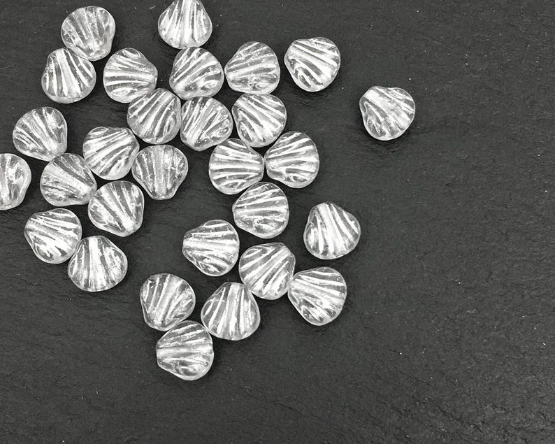 May include: A collection of clear, heart-shaped beads with a silver, striped design. The beads are scattered on a dark surface, showcasing their unique texture and shape. Ideal for jewelry making or craft projects.