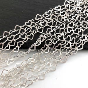 以下が含まれることがあります： 銀色のチェーンの複数のストランドのクローズアップ。各チェーンは、相互接続されたハート型のリンクで構成されており、繊細なオープンワークデザインを作成しています。チェーンはわずかに波状のパターンに配置され、ハートの形状の詳細を示しています。