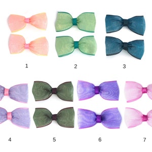Peut inclure: Une collection de sept paires de nœuds décoratifs de différentes couleurs. Les nœuds sont faits d'un matériau transparent et texturé avec une bande centrale contrastante. Les couleurs incluent pêche, vert, sarcelle, lavande, olive, violet et rose.