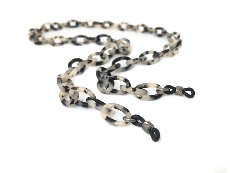 May include: A black and white tortoiseshell patterned plastic chain with black rubber ends for holding glasses.
